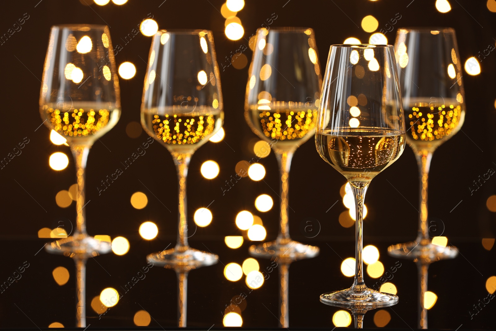 Photo of Tasty white wine in glasses on mirror surface against dark background with blurred lights. Bokeh effect