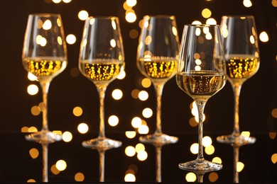 Photo of Tasty white wine in glasses on mirror surface against dark background with blurred lights. Bokeh effect