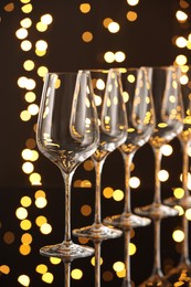 Photo of Empty wineglasses on mirror surface against dark background with blurred lights. Bokeh effect