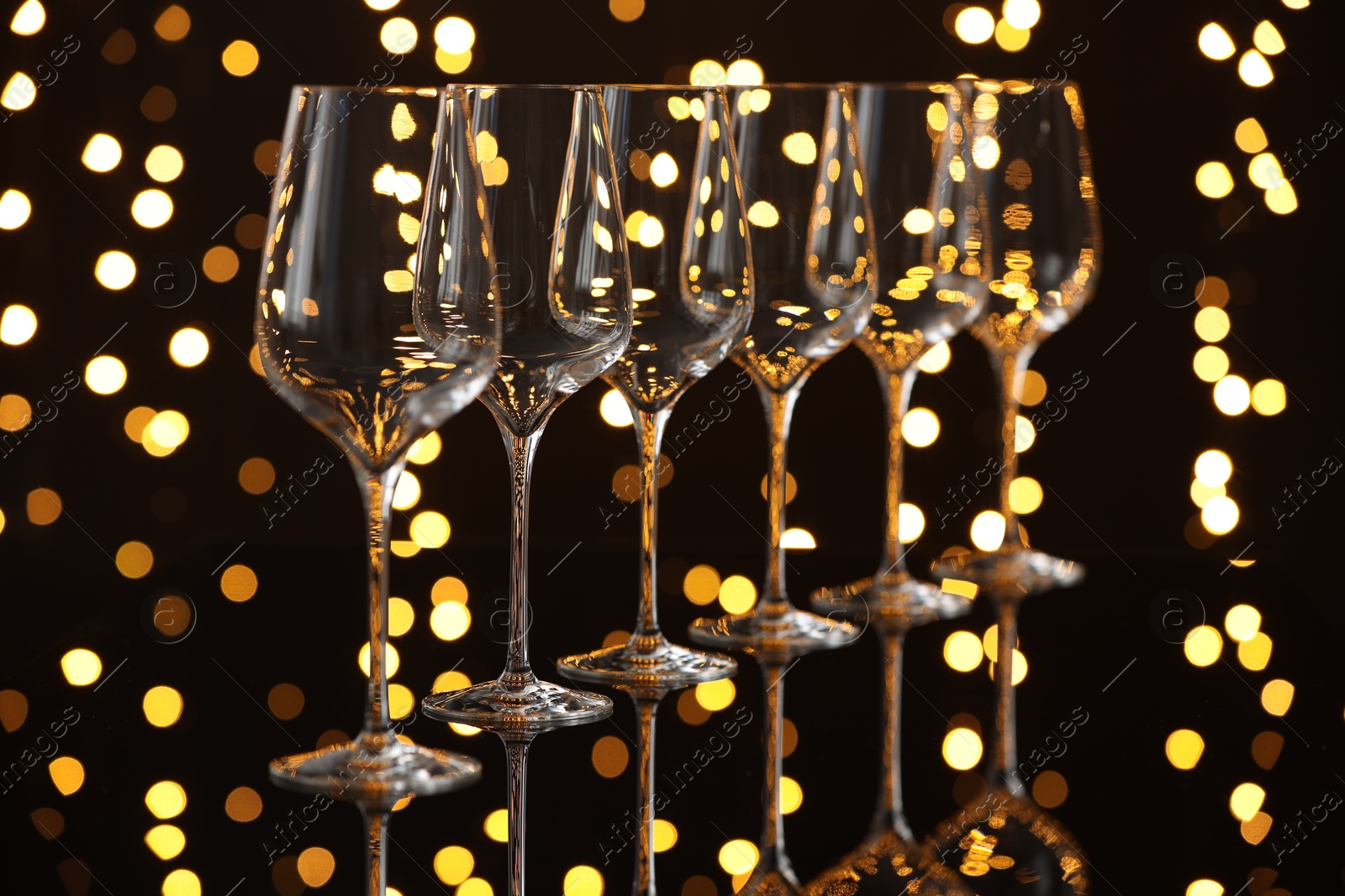 Photo of Empty wineglasses on mirror surface against dark background with blurred lights. Bokeh effect