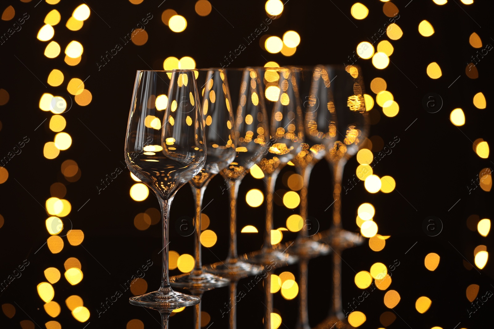 Photo of Empty wineglasses on mirror surface against dark background with blurred lights. Bokeh effect