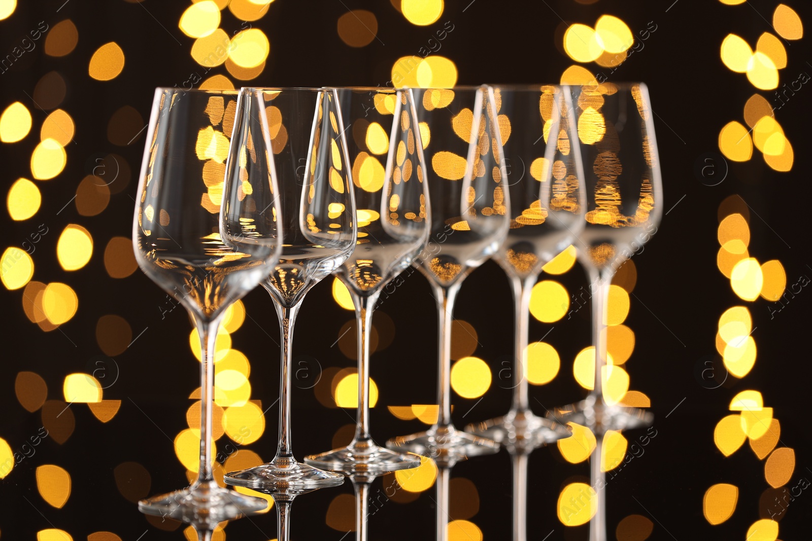 Photo of Empty wineglasses on mirror surface against dark background with blurred lights. Bokeh effect