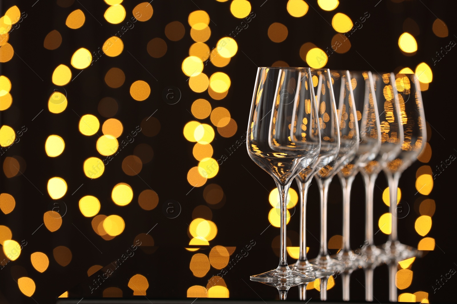 Photo of Empty wineglasses on mirror surface against dark background with blurred lights, space for text. Bokeh effect