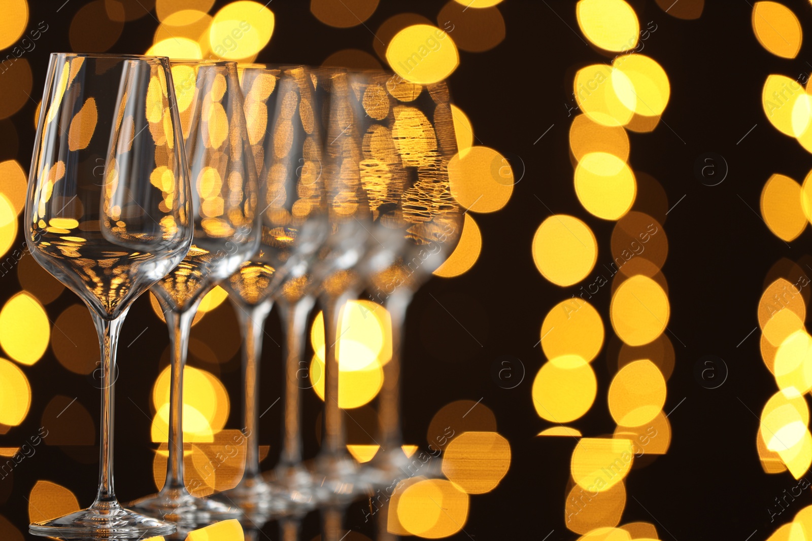 Photo of Empty wineglasses on mirror surface against dark background with blurred lights, space for text. Bokeh effect