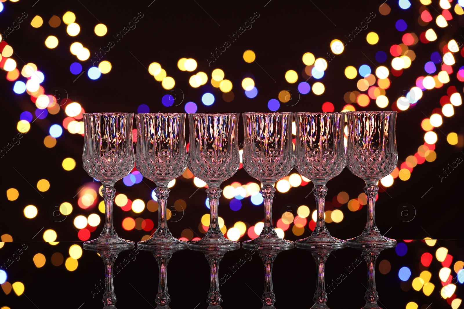 Photo of Empty wineglasses on mirror surface against black background with blurred lights, bokeh effect