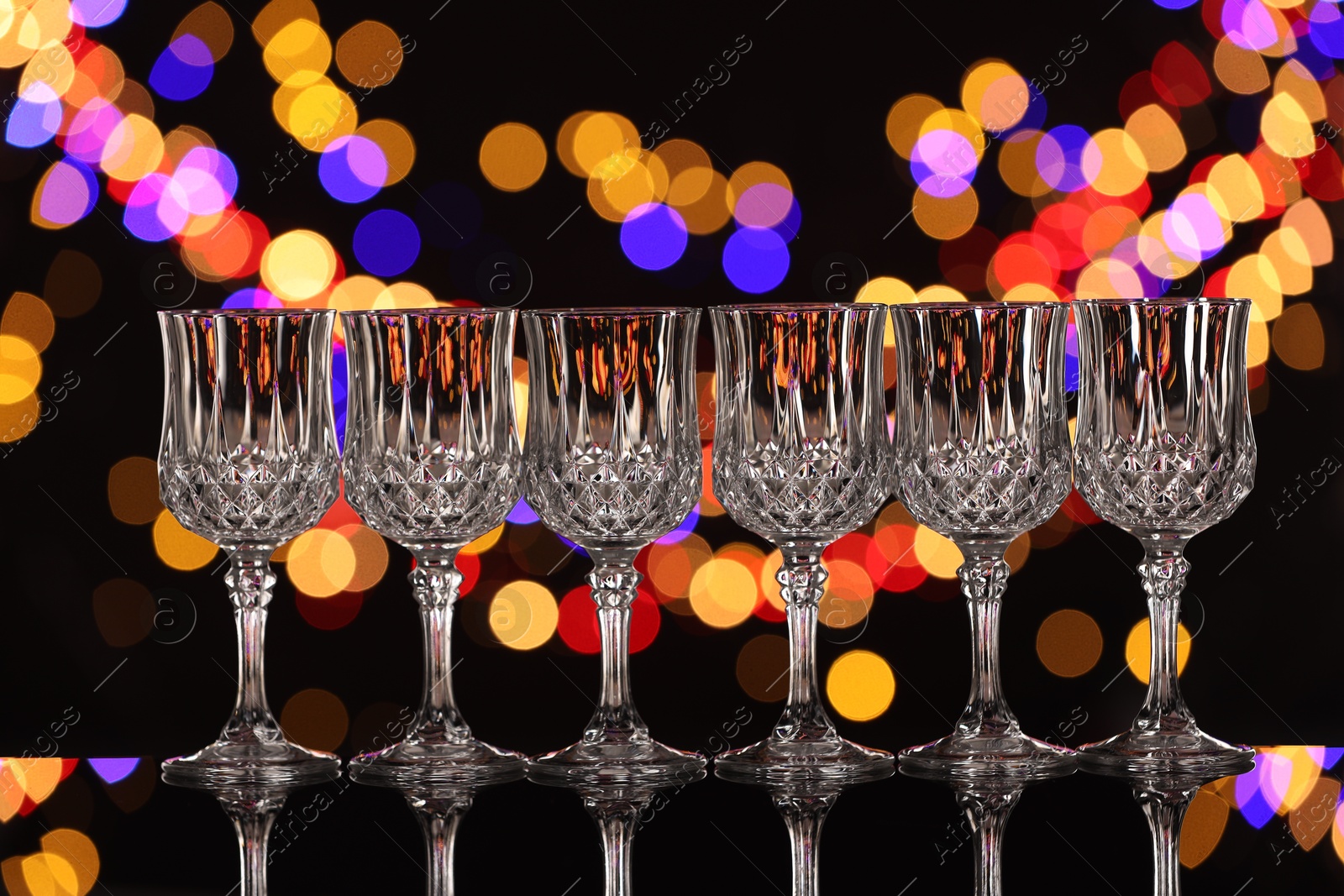 Photo of Empty wineglasses on mirror surface against black background with blurred lights, bokeh effect