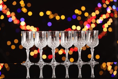 Photo of Empty wineglasses on mirror surface against black background with blurred lights, bokeh effect