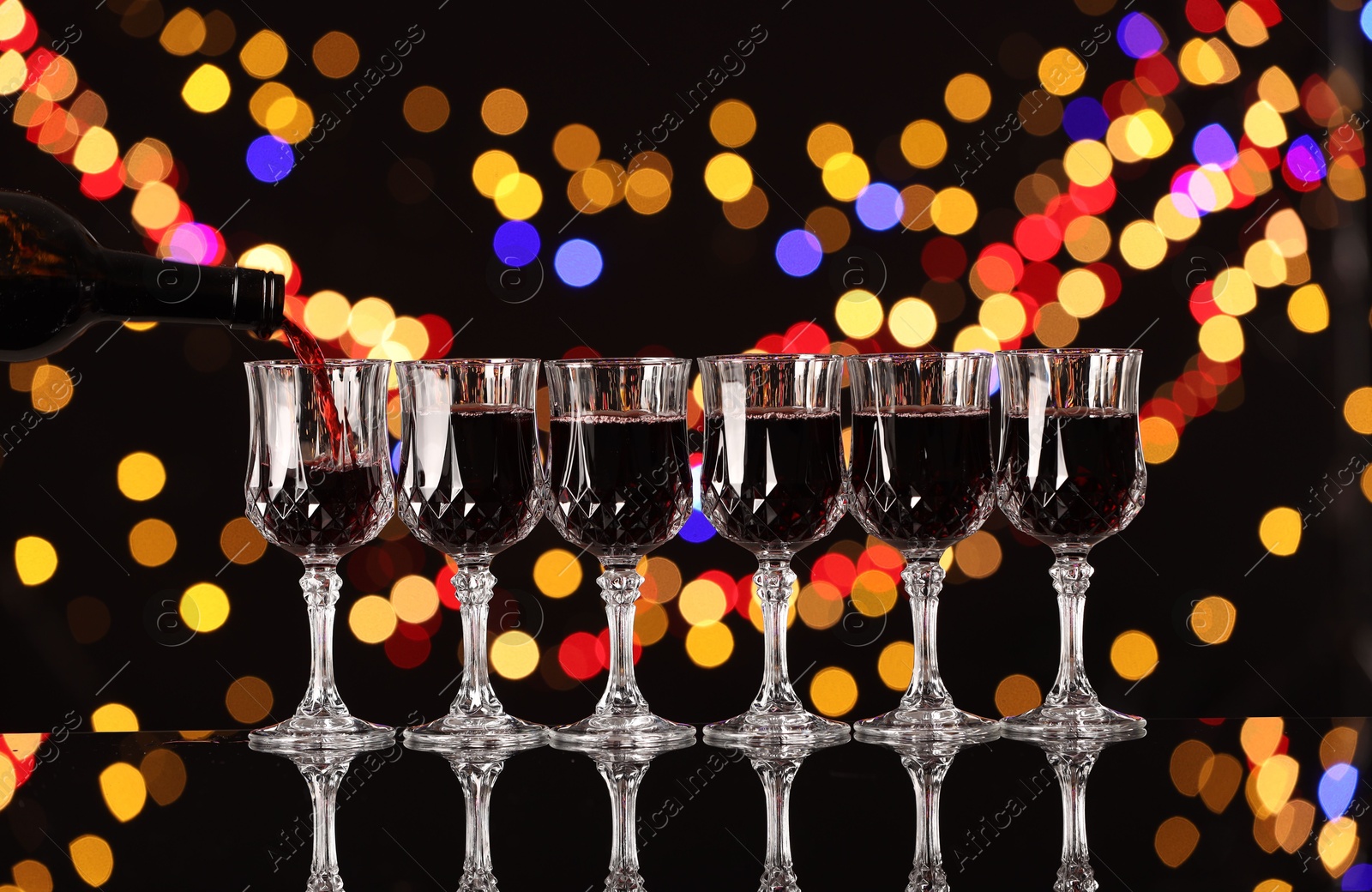 Photo of Pouring red wine into glass against black background with blurred lights. Bokeh effect