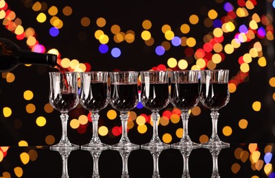 Photo of Pouring red wine into glass against black background with blurred lights. Bokeh effect