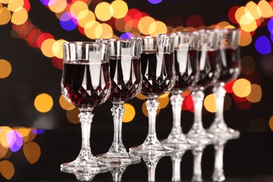 Photo of Tasty red wine in glasses on mirror surface against dark background with blurred lights, bokeh effect