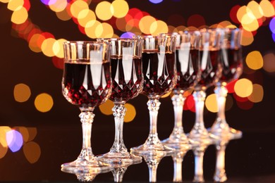 Photo of Tasty red wine in glasses on mirror surface against dark background with blurred lights, bokeh effect