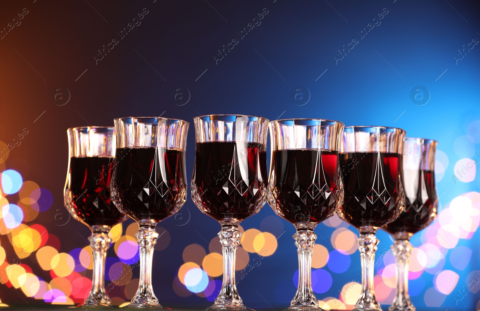 Photo of Tasty red wine in glasses against color background with blurred lights, low angle view. Bokeh effect