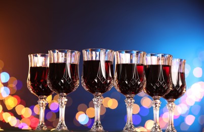 Photo of Tasty red wine in glasses against color background with blurred lights, low angle view. Bokeh effect