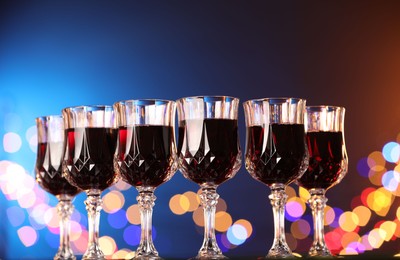 Photo of Tasty red wine in glasses against color background with blurred lights, low angle view. Bokeh effect