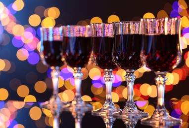 Photo of Tasty red wine in glasses on mirror surface against dark background with blurred lights, bokeh effect