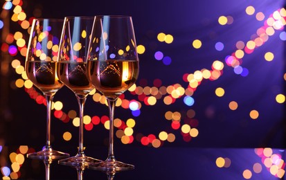 Photo of Tasty white wine in glasses on mirror surface against dark purple background with blurred lights, space for text. Bokeh effect