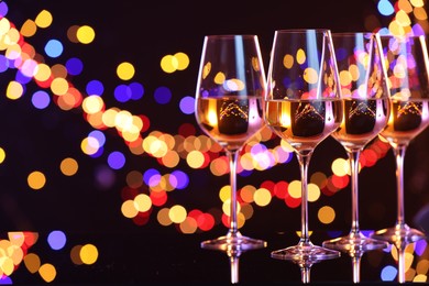 Photo of Tasty white wine in glasses on mirror surface against dark background with blurred lights, space for text. Bokeh effect