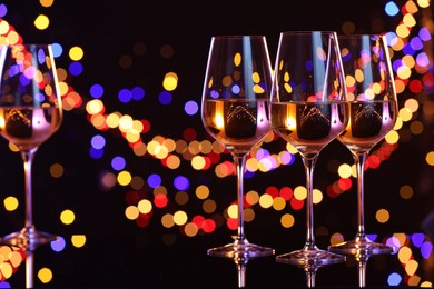 Photo of Tasty white wine in glasses on mirror surface against dark background with blurred lights, bokeh effect