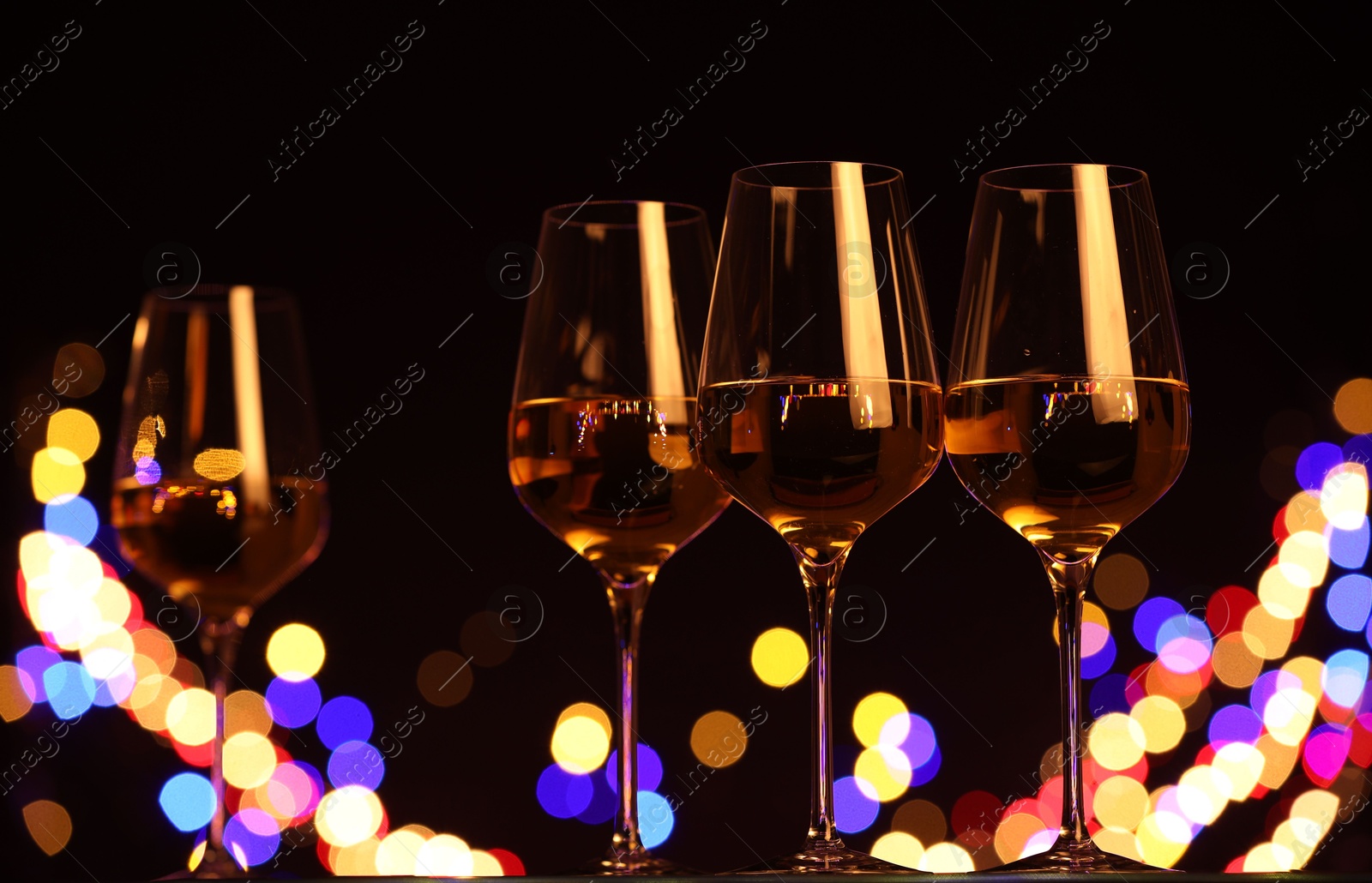 Photo of Tasty white wine in glasses against black background with blurred lights, low angle view. Bokeh effect