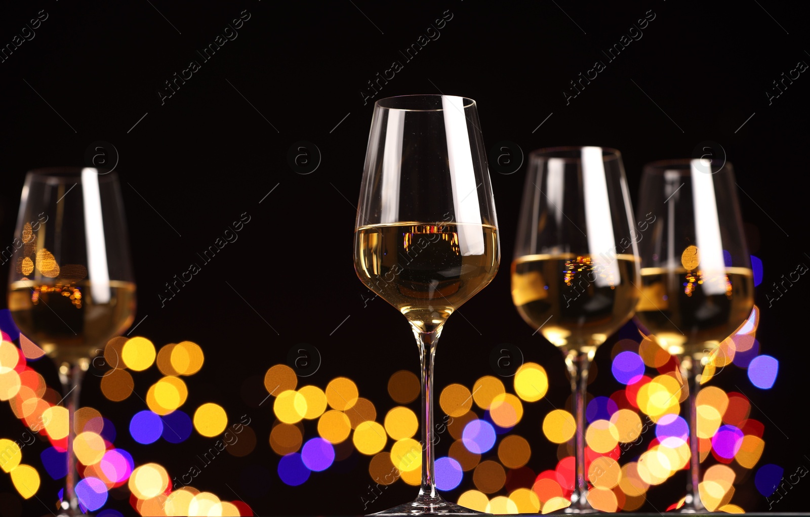 Photo of Tasty white wine in glasses against black background with blurred lights, low angle view. Bokeh effect