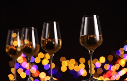 Photo of Tasty white wine in glasses against black background with blurred lights, low angle view. Bokeh effect