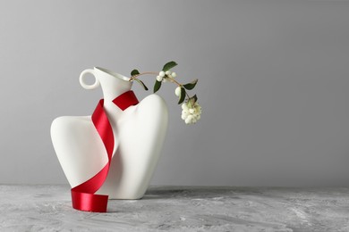 Photo of Stylish vase with snowberry branch and red ribbon on grey table, space for text