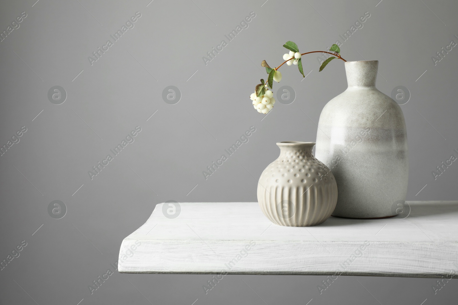 Photo of Stylish vases and snowberry branch on white table, space for text