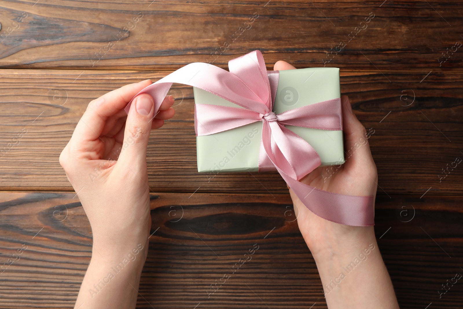 Photo of Woman holding gift box with pink bow on wooden table, top view