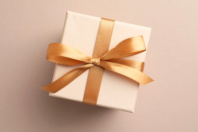 Photo of Gift box with golden bow on beige background, top view