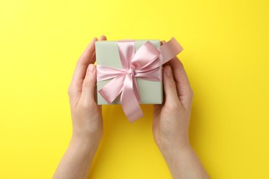 Photo of Woman holding gift box with pink bow on yellow background, top view