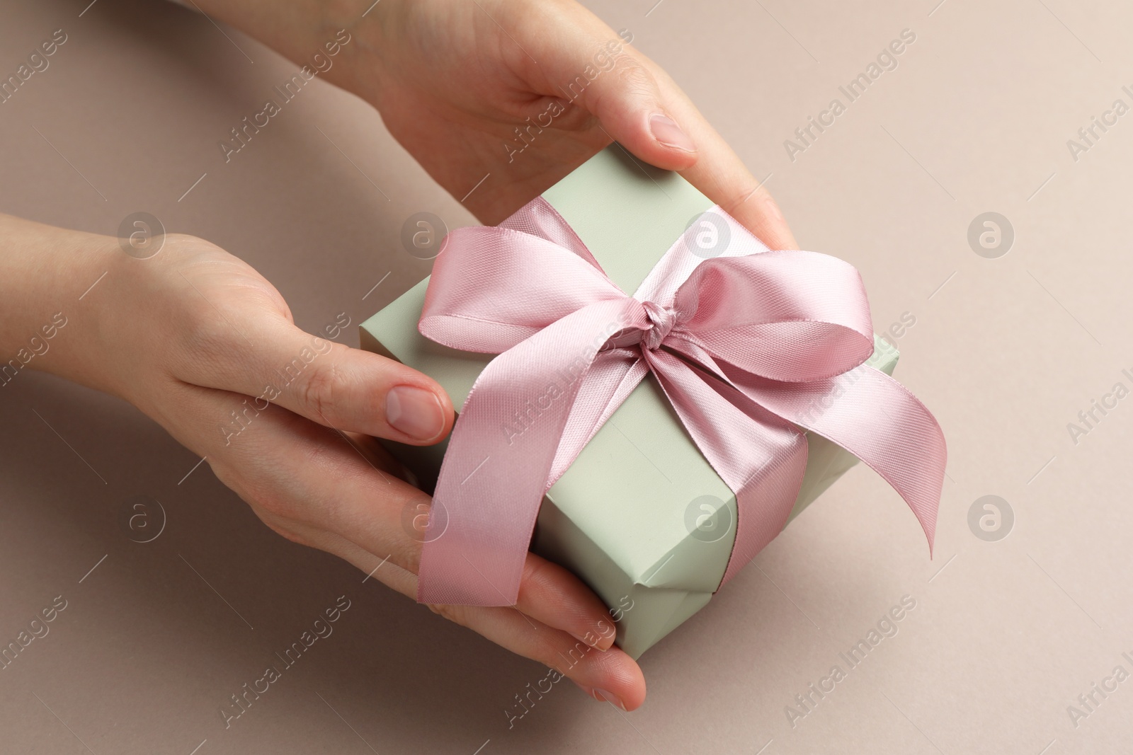 Photo of Woman holding gift box with pink bow on beige background, closeup