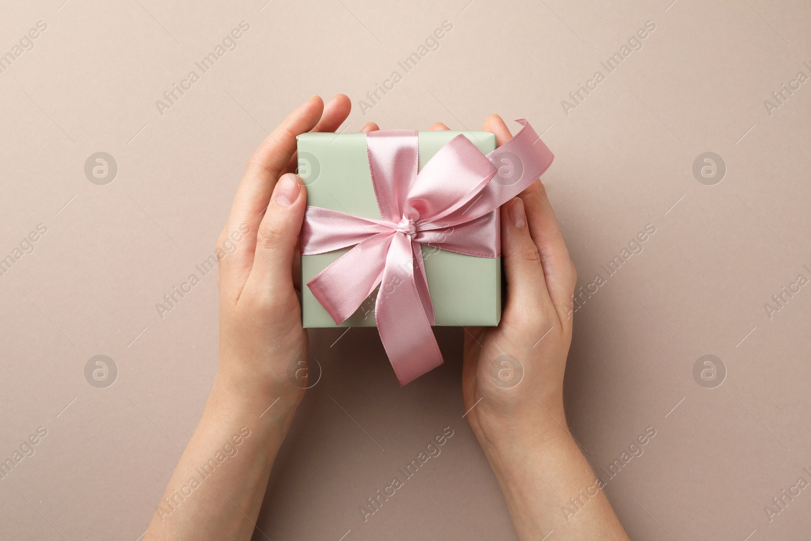 Photo of Woman holding gift box with pink bow on beige background, top view