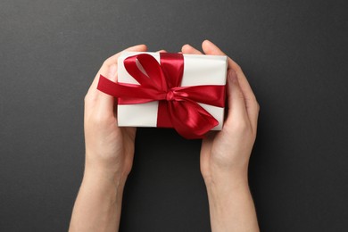 Photo of Woman holding gift box with red bow on black background, top view