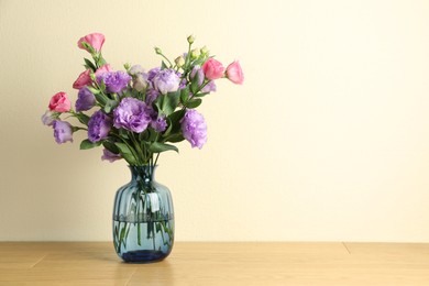 Photo of Vase with beautiful eustoma flowers on wooden table, space for text