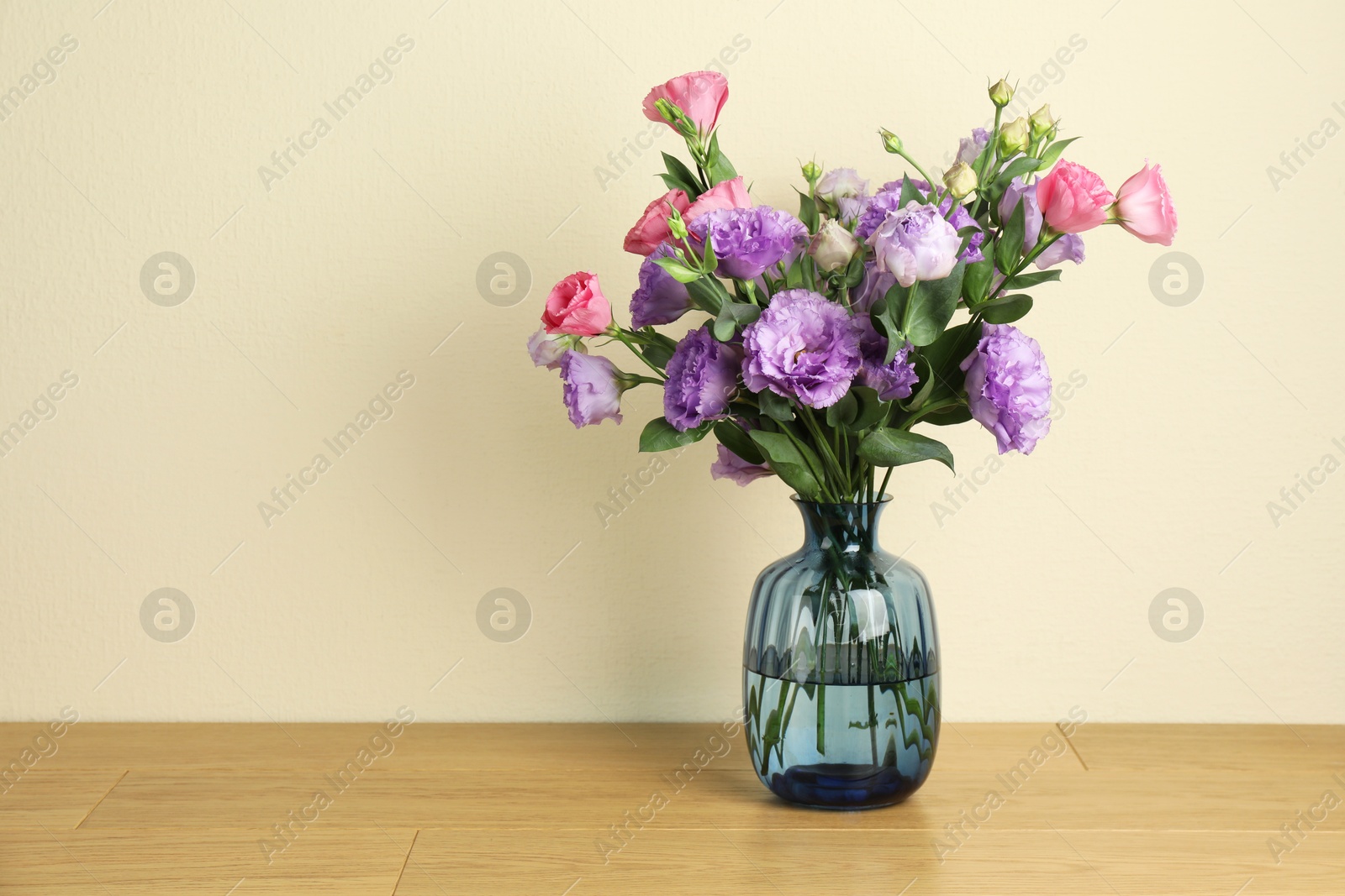 Photo of Vase with beautiful eustoma flowers on wooden table, space for text