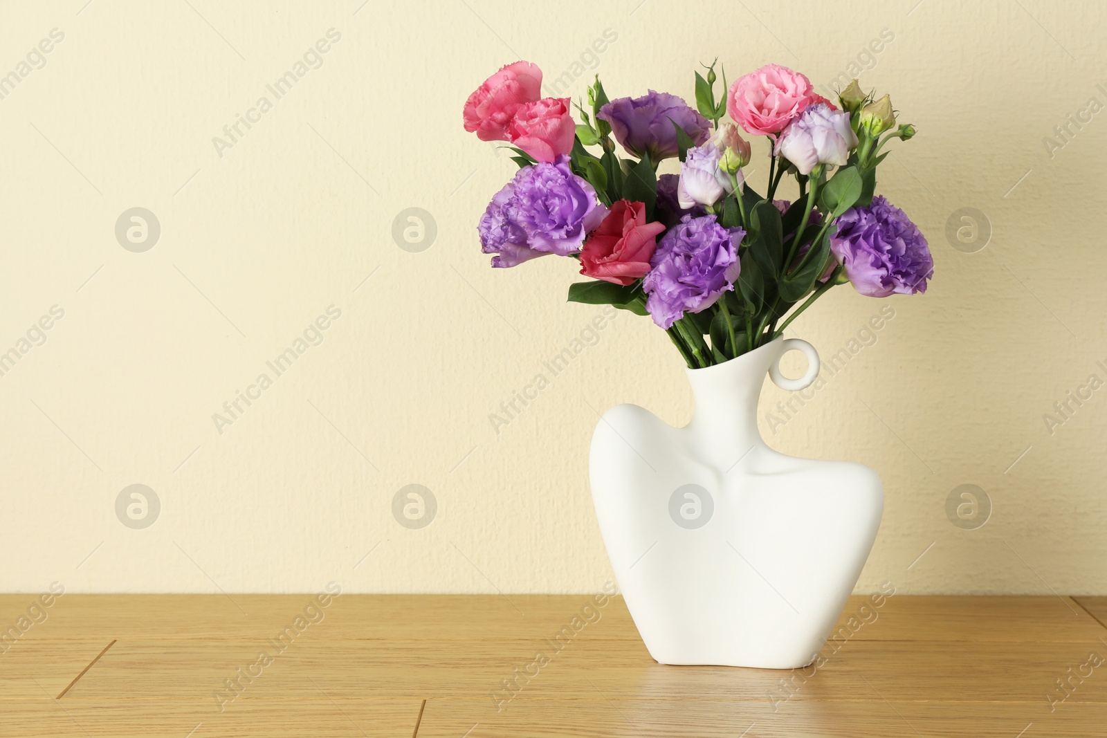 Photo of Vase with beautiful eustoma flowers on wooden table, space for text