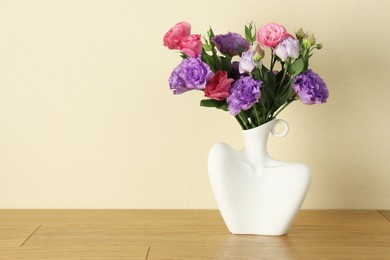 Photo of Vase with beautiful eustoma flowers on wooden table, space for text