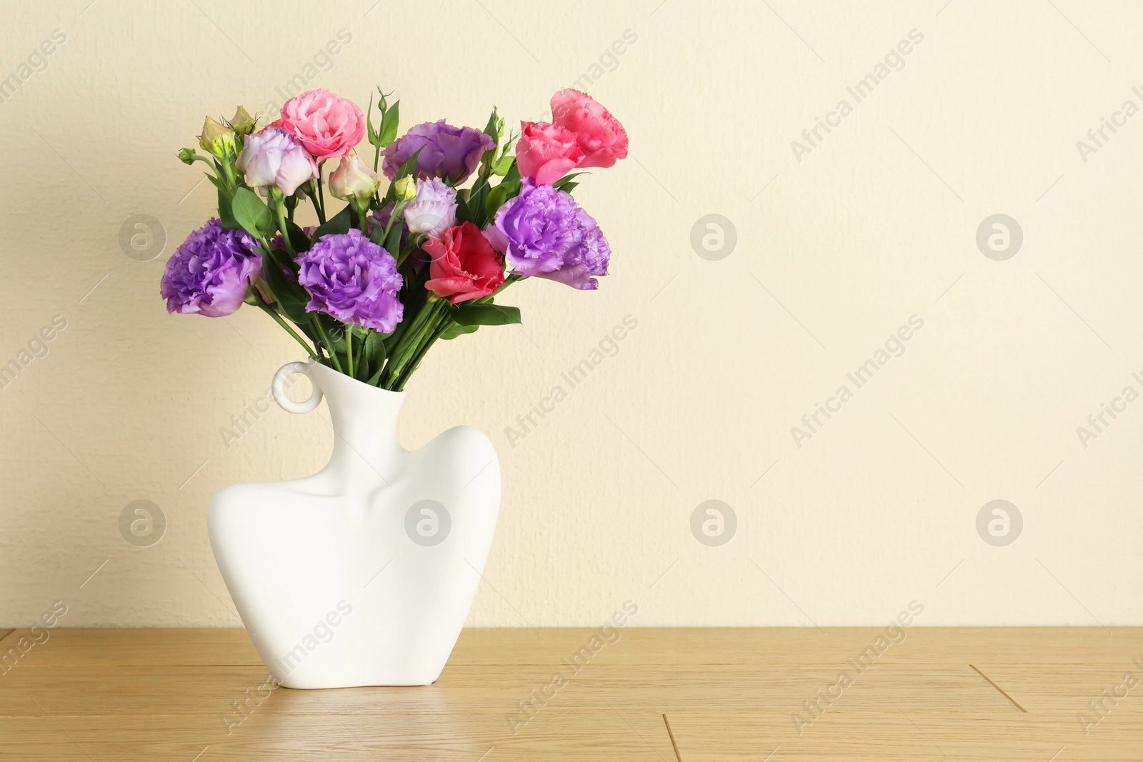 Photo of Vase with beautiful eustoma flowers on wooden table, space for text