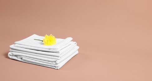 Stack of clean bed linens and beautiful flower on beige background, space for text