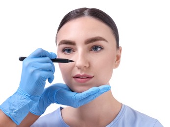 Doctor drawing marks on patient's nose for plastic surgery operation against white background, closeup