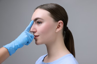 Photo of Doctor checking patient's nose before plastic surgery operation on grey background, closeup