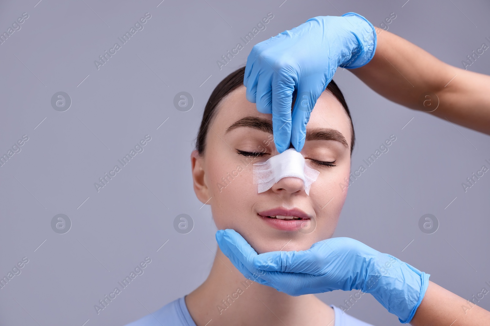 Photo of Doctor checking patient's nose after plastic surgery operation on grey background, closeup. Space for text