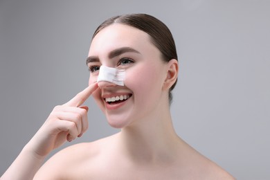 Photo of Woman with medical bandage on her nose after plastic surgery operation against grey background