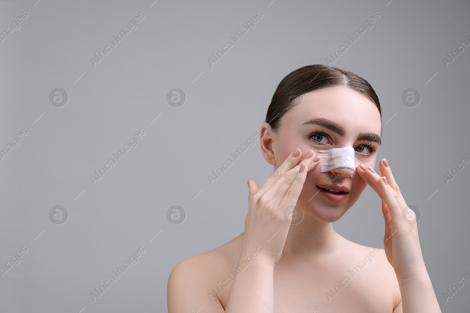 Photo of Woman with medical bandage on her nose after plastic surgery operation against grey background, space for text