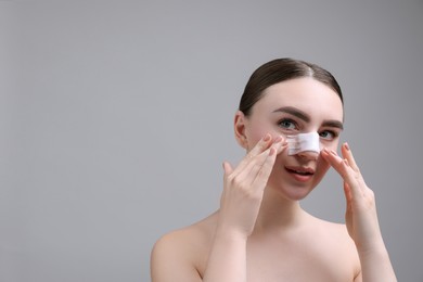 Woman with medical bandage on her nose after plastic surgery operation against grey background, space for text