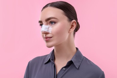 Photo of Woman with medical bandage on her nose after plastic surgery operation against pink background