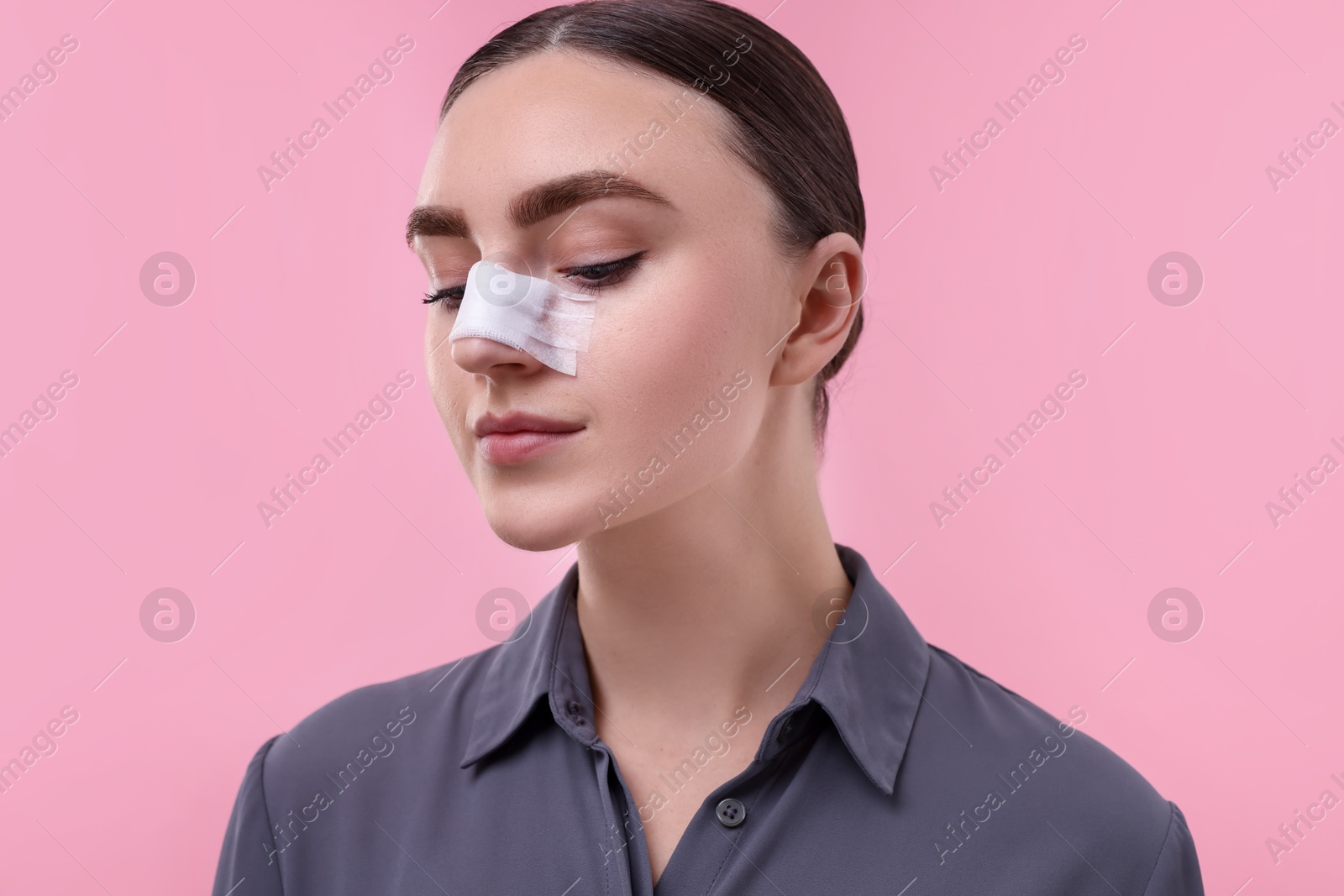 Photo of Woman with medical bandage on her nose after plastic surgery operation against pink background