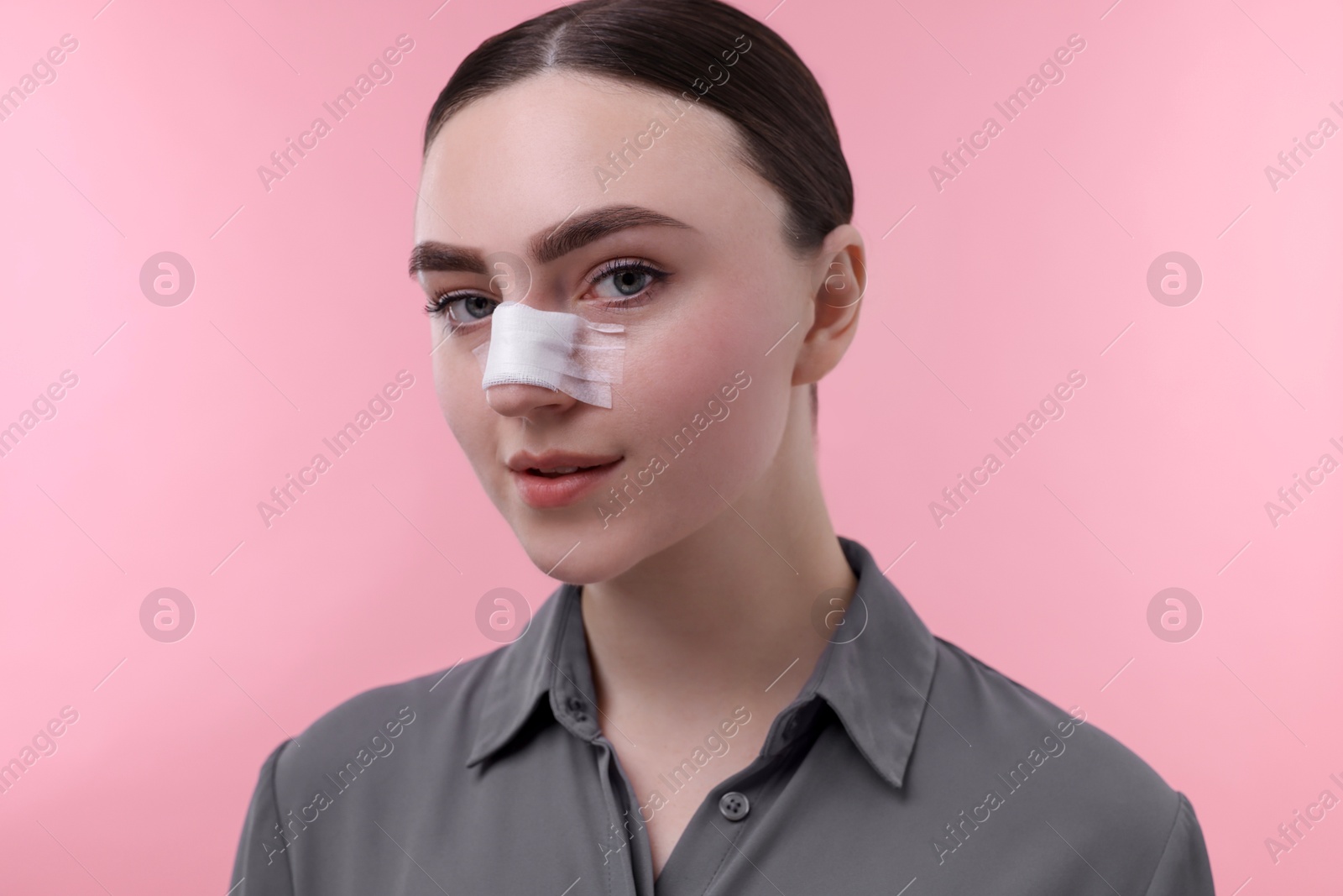 Photo of Woman with medical bandage on her nose after plastic surgery operation against pink background