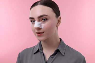 Woman with medical bandage on her nose after plastic surgery operation against pink background