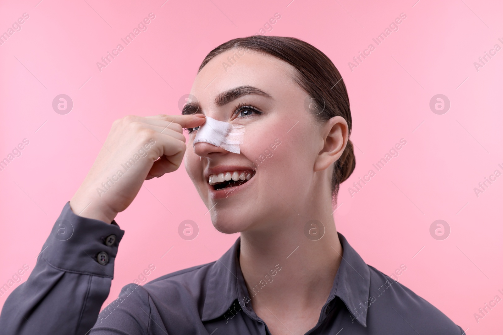 Photo of Woman with medical bandage on her nose after plastic surgery operation against pink background